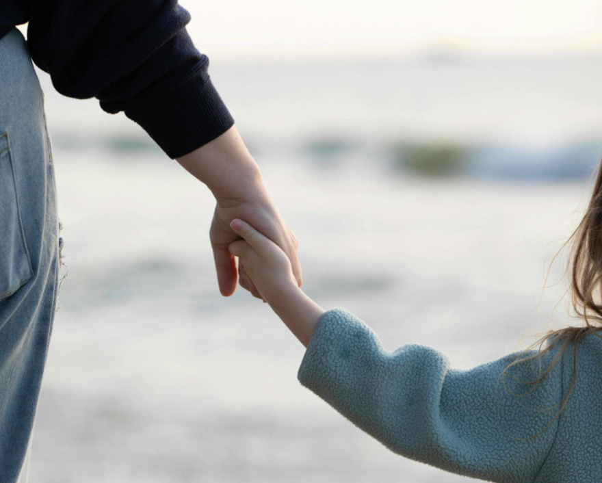 Close up of a mother and young daughter holding hands while looking at the ocean