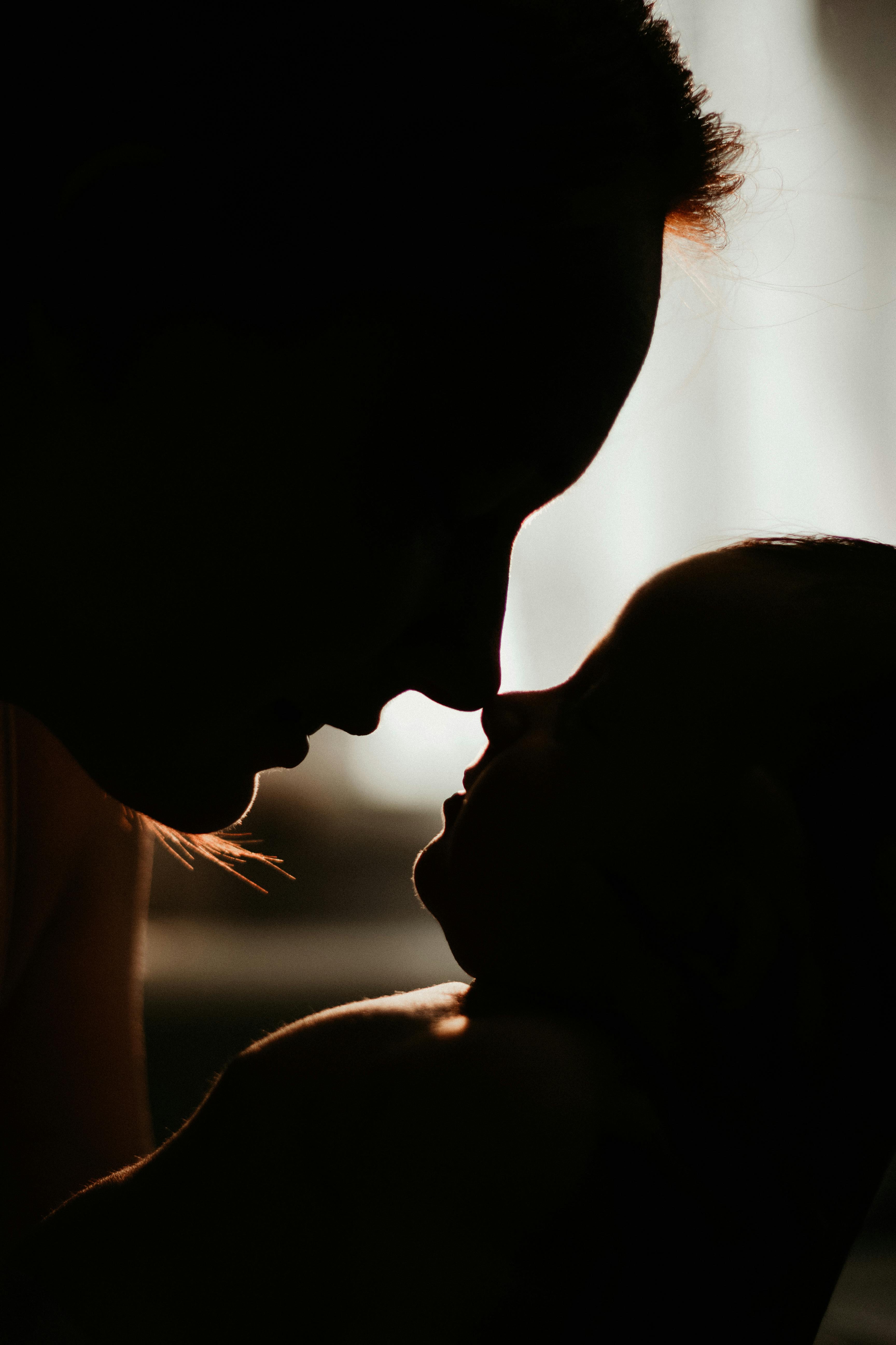 A close up silhouette of a mother holding an infant as their noses touch