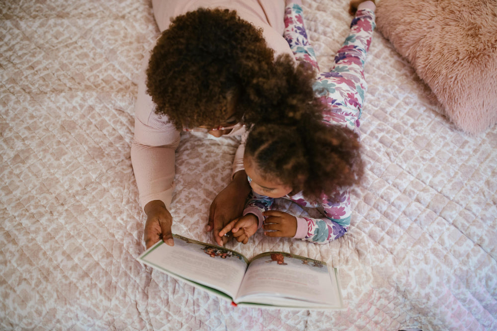 An overhead view of a mother and young daughter in pajamas reading a book together on a bed